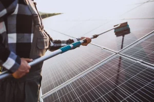 Homme en train de nettoyer ses panneaux solaires à l'aide d'une brosse téléscopique